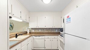 Una cocina con armarios blancos, lavavajillas, refrigerador y salpicadero de azulejos.