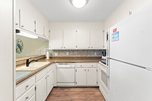 A kitchen with white cabinets, a dishwasher, a refrigerator, and a tiled backsplash.