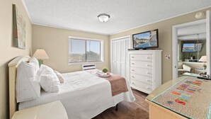 Un dormitorio con cama, cómoda, televisor y vista a una piscina por la ventana.