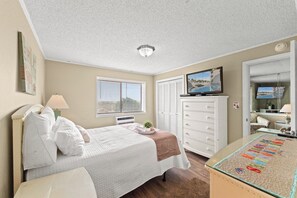 A bedroom with a bed, a dresser, a television, and a view of a swimming pool through the window.