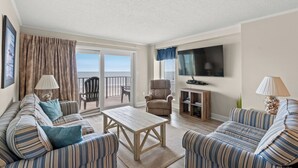 A living room with striped sofas, a wooden coffee table, a TV, and a balcony with a view. - Tidemaster 402-3BR/3BA Oceanfront condo in Ocean Drive (North Myrtle Beach)