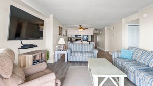 A living room with a sofa, a coffee table, a TV, and a kitchen area in the background. - Tidemaster 402-3BR/3BA Oceanfront condo in Ocean Drive (North Myrtle Beach)