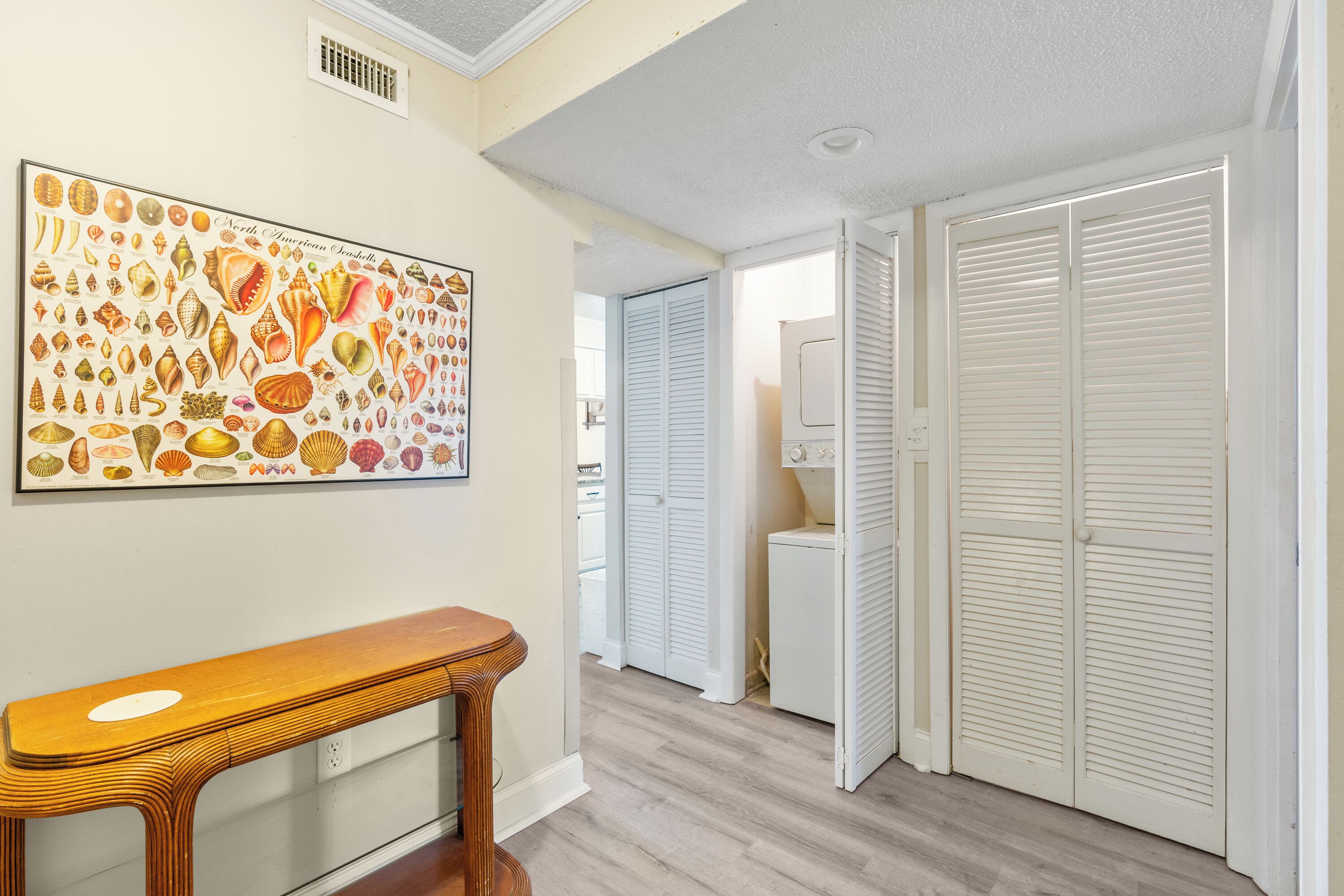 A hallway with a wooden bench, a large marine shell artwork, and white louvered closets.