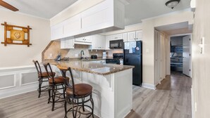 A spacious kitchen with white cabinetry, a granite countertop, and a central island with bar stools. - Tidemaster 402-3BR/3BA Oceanfront condo in Ocean Drive (North Myrtle Beach)