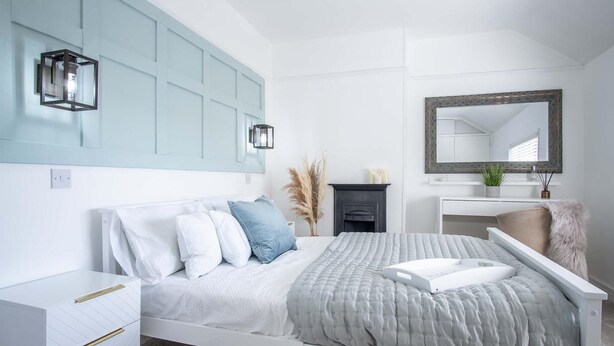 A modern bedroom with a white bed, a nightstand, a dresser, a mirror, and a fireplace.