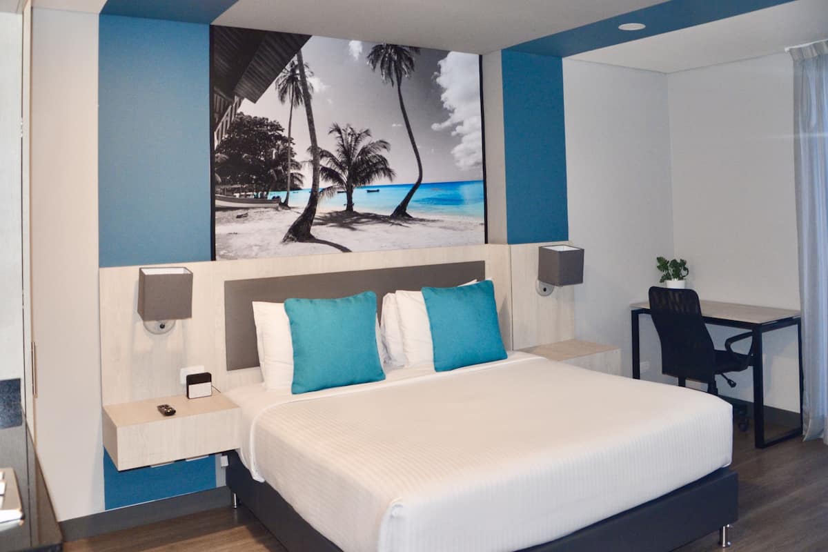 A hotel room with a large bed, a desk, and a painting of a beach scene.