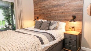 A bedroom with a wooden headboard, a bed with striped bedding, two bedside lamps, and a nightstand with drawers. - Lavender Lodge (Gunnislake)