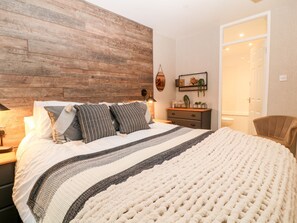 A bedroom with a wooden headboard, a bed with striped bedding, a bedside table with a lamp, a dresser, and a door leading to a bathroom. - Lavender Lodge (Gunnislake)