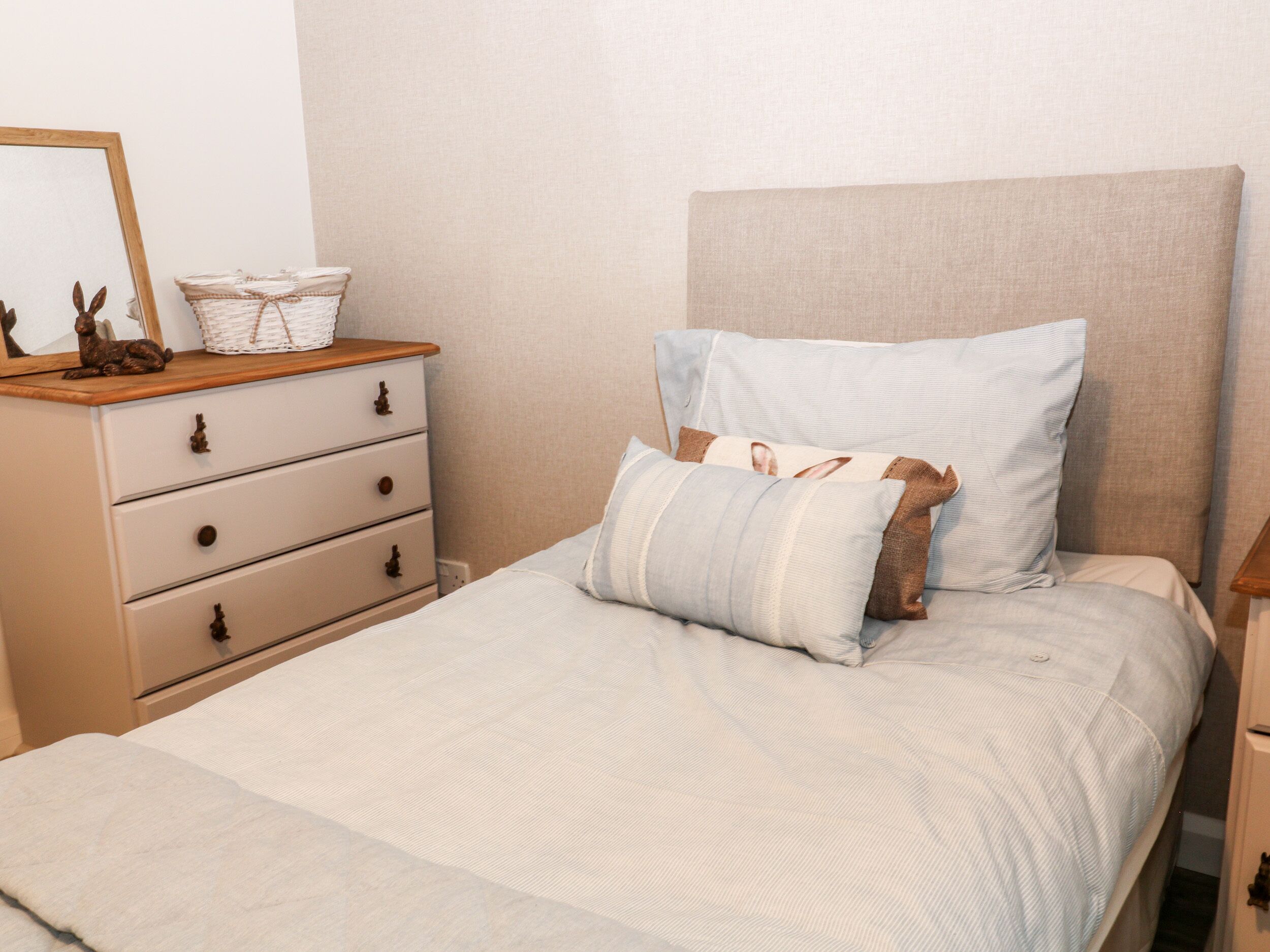 A neatly made bed with a striped bedspread and two pillows, a wooden dresser with drawers, and a mirror on the dresser.