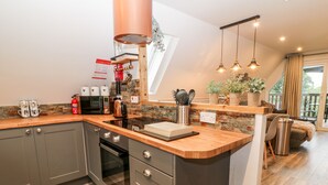 A modern kitchen with grey cabinets, a wooden countertop, and stainless steel appliances. There is a fire extinguisher, a kettle, and a coffee maker on the counter. The kitchen leads to a dining area with a view of the outdoors. - Lavender Lodge (Gunnislake)