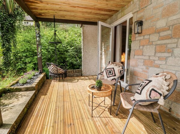 Une terrasse extérieure dotée d’un plancher en bois, de meubles en osier et d’un fauteuil suspendu.