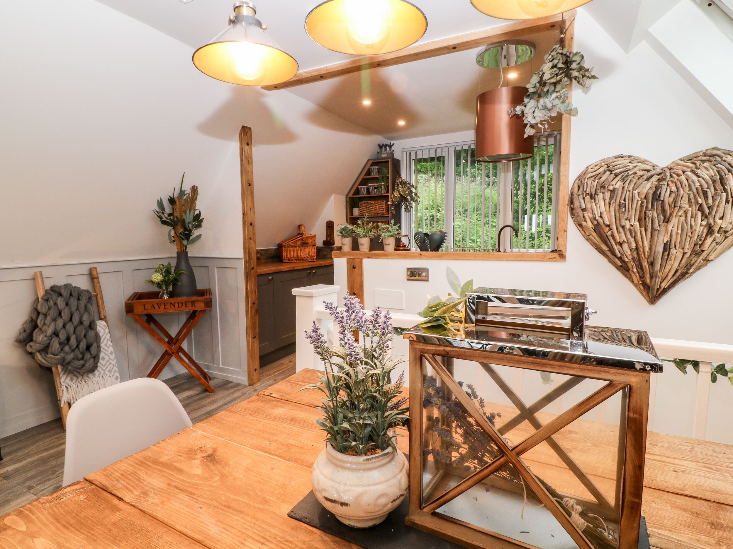 A dining area with a wooden table, a white chair, a vase with flowers, and a heart-shaped wall decoration.