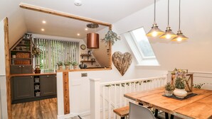 A compact kitchen with a wooden beam ceiling, a heart-shaped wall decoration, and a dining area with a wooden table and chairs. - Lavender Lodge (Gunnislake)