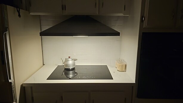 Uma cozinha com um exaustor preto, uma chaleira e um pequeno recipiente na bancada.