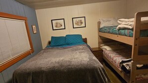 Quarto com uma cama de solteiro, beliches, janela com persianas e duas imagens emolduradas na parede.
