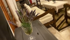 A room with a dining table set for two, a fireplace, and a bed with a white comforter. - Cosy Calm Cottage in Olive Trees With sea View (Ermionida)