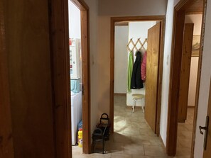 A hallway with a wooden door frame, a coat rack with jackets, a small stool, and a suitcase on the floor. - Cosy Calm Cottage in Olive Trees With sea View (Ermionida)