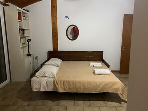 A bedroom with a bed, a wardrobe, a mirror, and a shelf with books and a lamp. - Cosy Calm Cottage in Olive Trees With sea View (Ermionida)