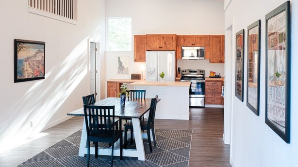 A modern kitchen with wooden cabinets, a central island, and a dining area with a table and chairs. - Beautiful new guest cottage, perfect for families! (Hayden)