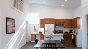 A modern kitchen with wooden cabinets, a central island, and a dining area with a table and chairs. - Beautiful new guest cottage, perfect for families! (Hayden)