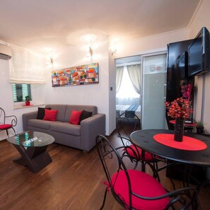 A modern living room with a grey sofa, red cushions, a glass coffee table, and a dining area with a round table and red chairs.