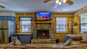 Una sala de estar acogedora con una chimenea de piedra, un televisor montado arriba y una zona de estar confortable con sofás de cuero.