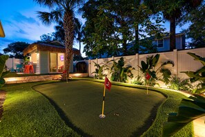 Un jardin bien entretenu avec un green d’entraînement au golf, un petit kiosque et une clôture blanche.