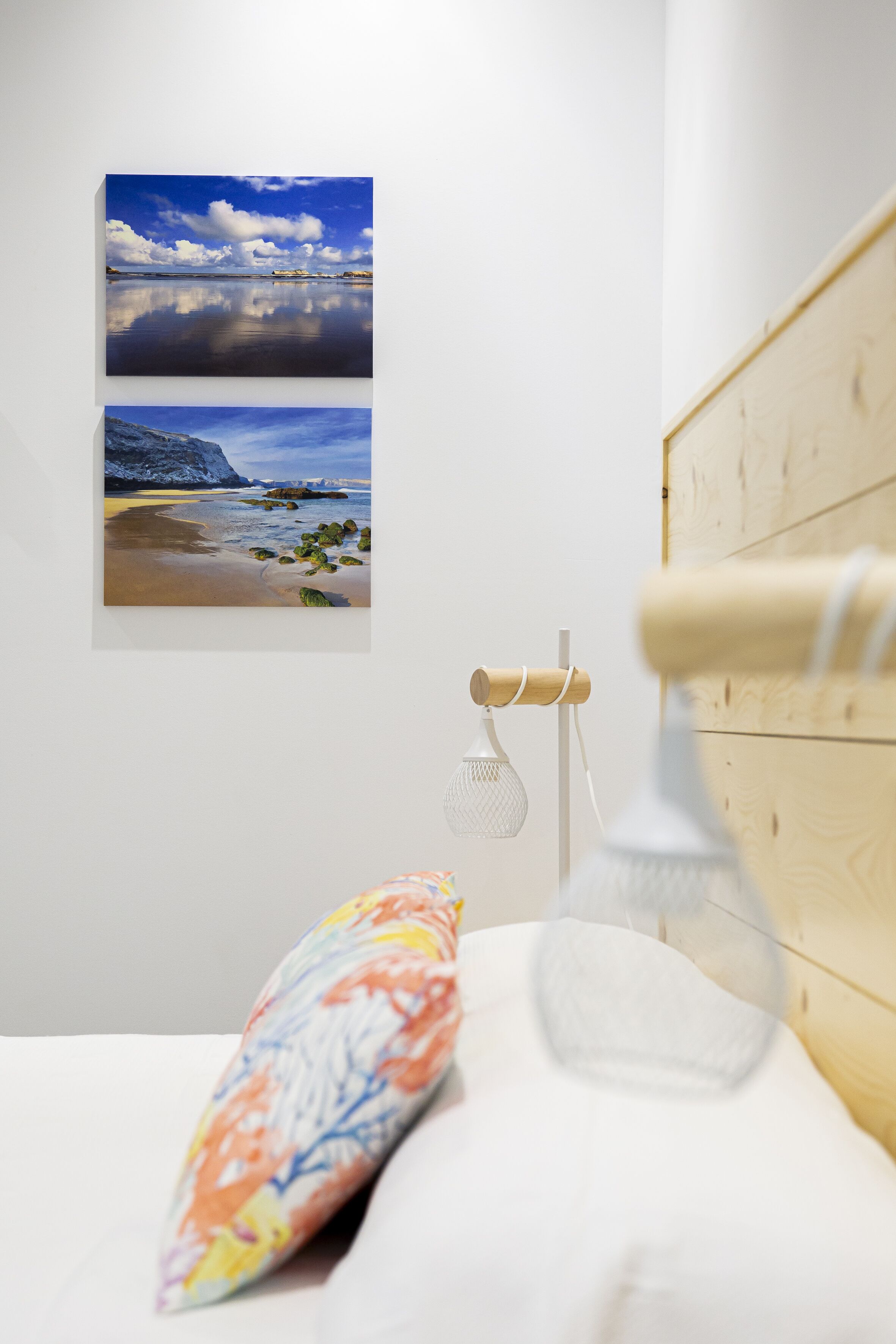 A bedroom with a bed, a pillow, a wall-mounted lamp, and two framed pictures of landscapes.