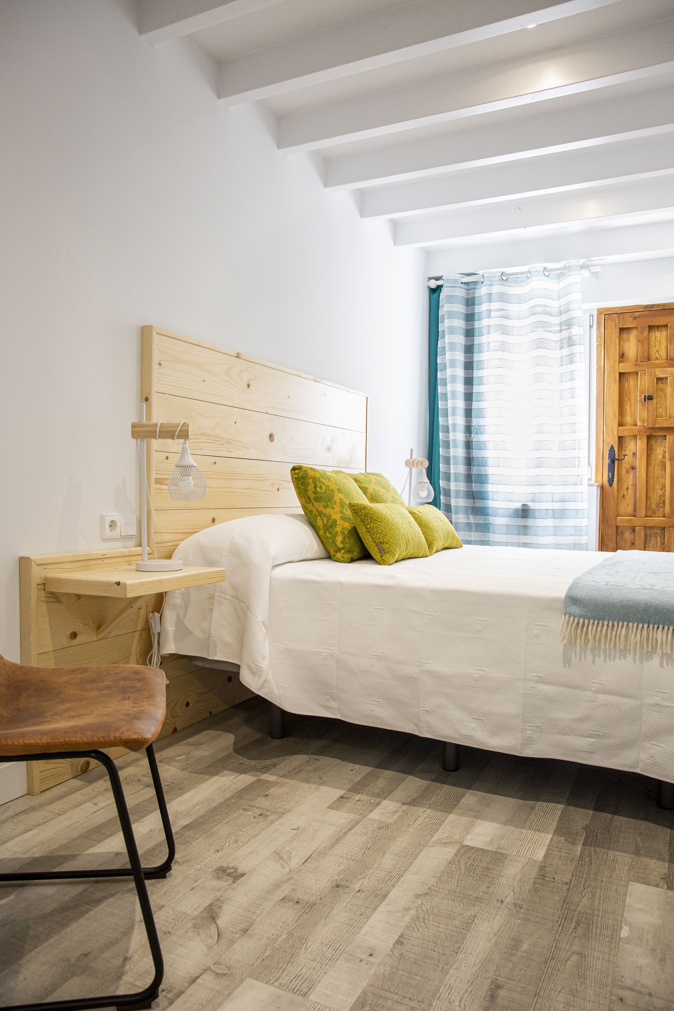 Une chambre à coucher avec une tête de lit en bois, un lit avec une literie blanche, une table de chevet avec une lampe et une chaise.