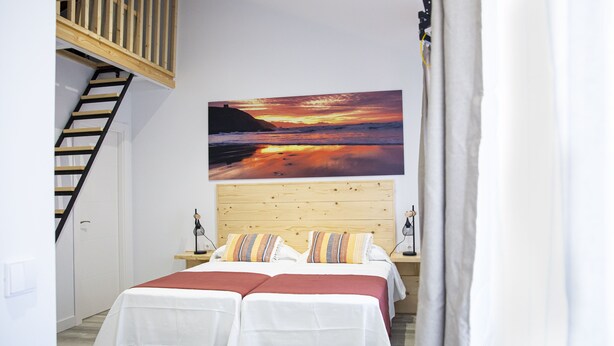 A bedroom with a wooden headboard, two beds with white bedding, a nightstand, and a painting of a sunset over the ocean. - Hotel la Caracola Suances (Suances)