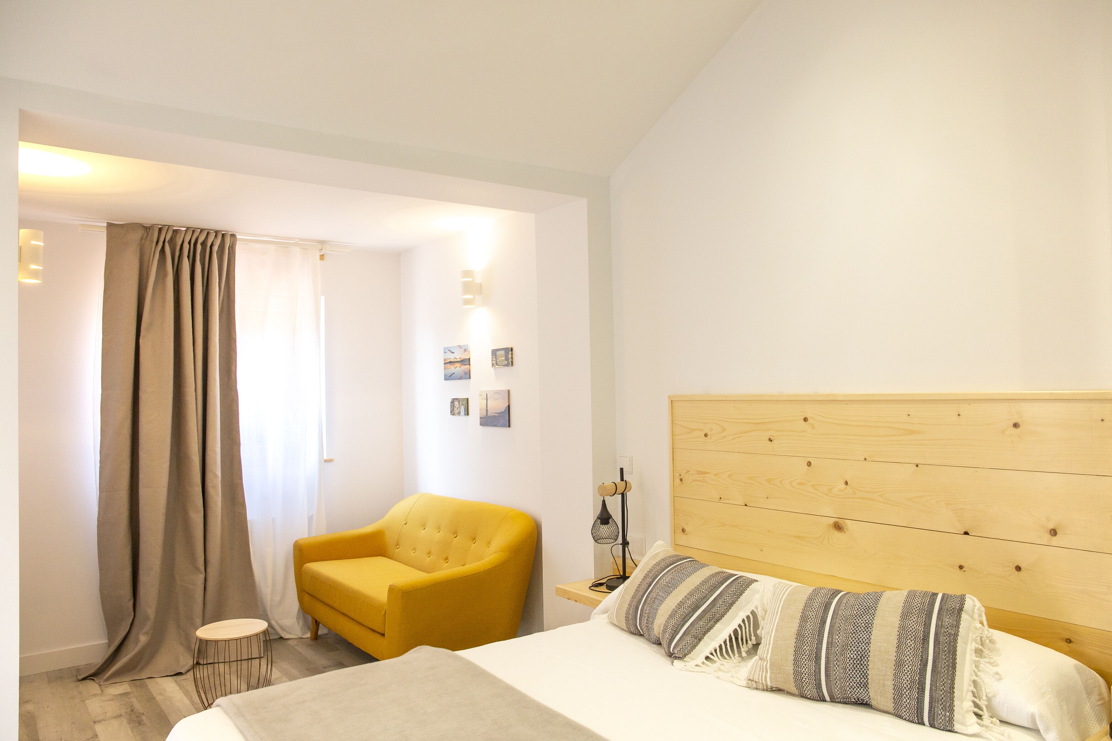 Un dormitorio con cama, un sillón amarillo, una mesita redonda y cabecera de madera.