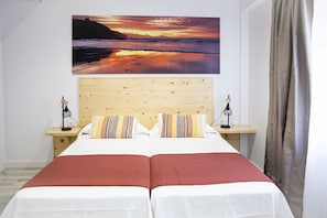 A double bed with two nightstands, a wooden headboard, and a painting of a sunset over the ocean. - Hotel la Caracola Suances (Suances)