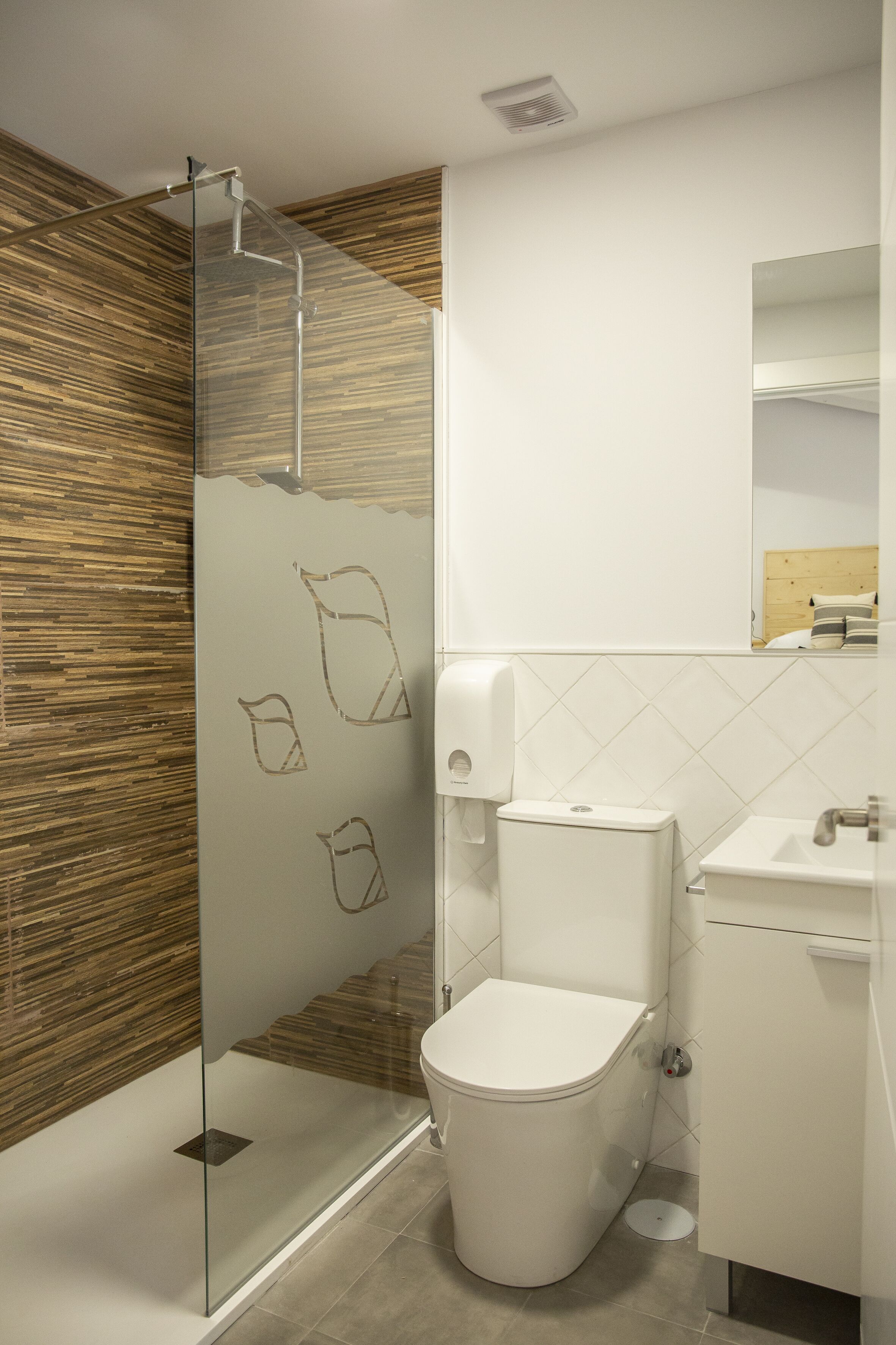 A modern bathroom with a glass shower enclosure, a toilet, a sink, and a mirror.