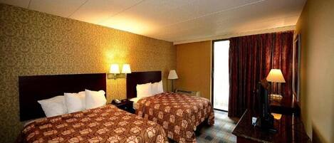 A hotel room with two beds, a desk, and a window with curtains.
