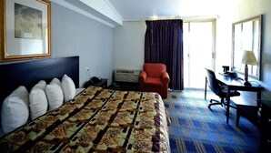 Ein Hotelzimmer mit einem großen Bett, einem Schreibtisch, einem Sessel und einem fenster mit Vorhängen.