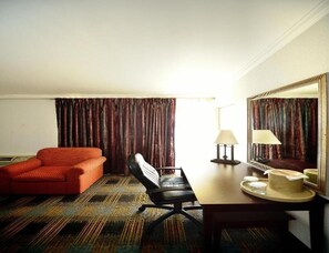 A hotel room with a red sofa, a black office chair, a wooden desk with a lamp, a tray with a cup and a plate, and a large mirror on the wall. - River-view Room, 1 King Bed with Jacuzzi tub and Balcony (Somerset)