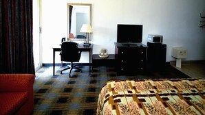 Une chambre d’hôtel comprenant un lit, un bureau avec une lampe, une télévision et une commode.