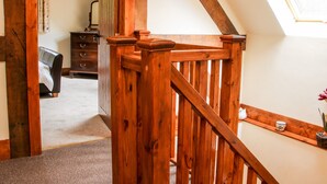 Un escalier en bois avec une rampe, une chambre à coucher avec un lit et une commode, et une fenêtre donnant sur un paysage verdoyant.