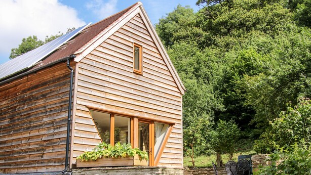 Une cabane en bois avec des fondations en pierre, de grandes fenêtres et un petit espace porche.