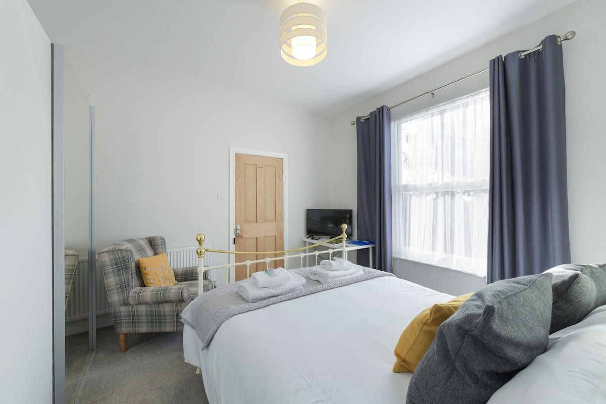 A bedroom with a bed, a chair, a television, and a window with curtains.