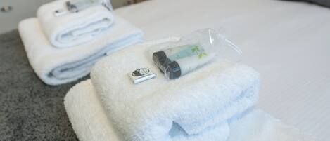A neatly folded white towel with a bottle and a small item on top, placed on a grey carpeted floor.