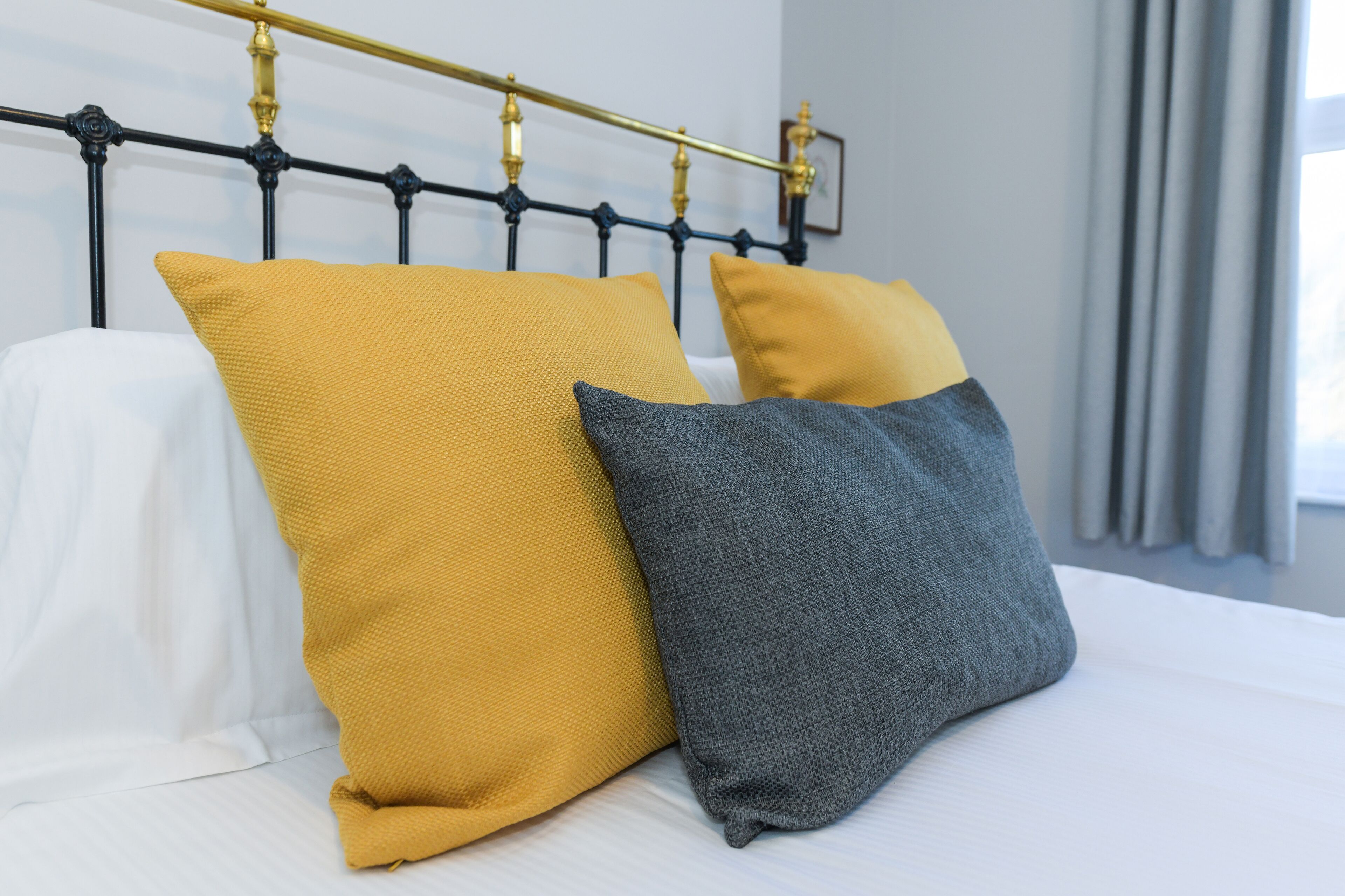A bed with a black metal headboard and two pillows, one yellow and one gray.