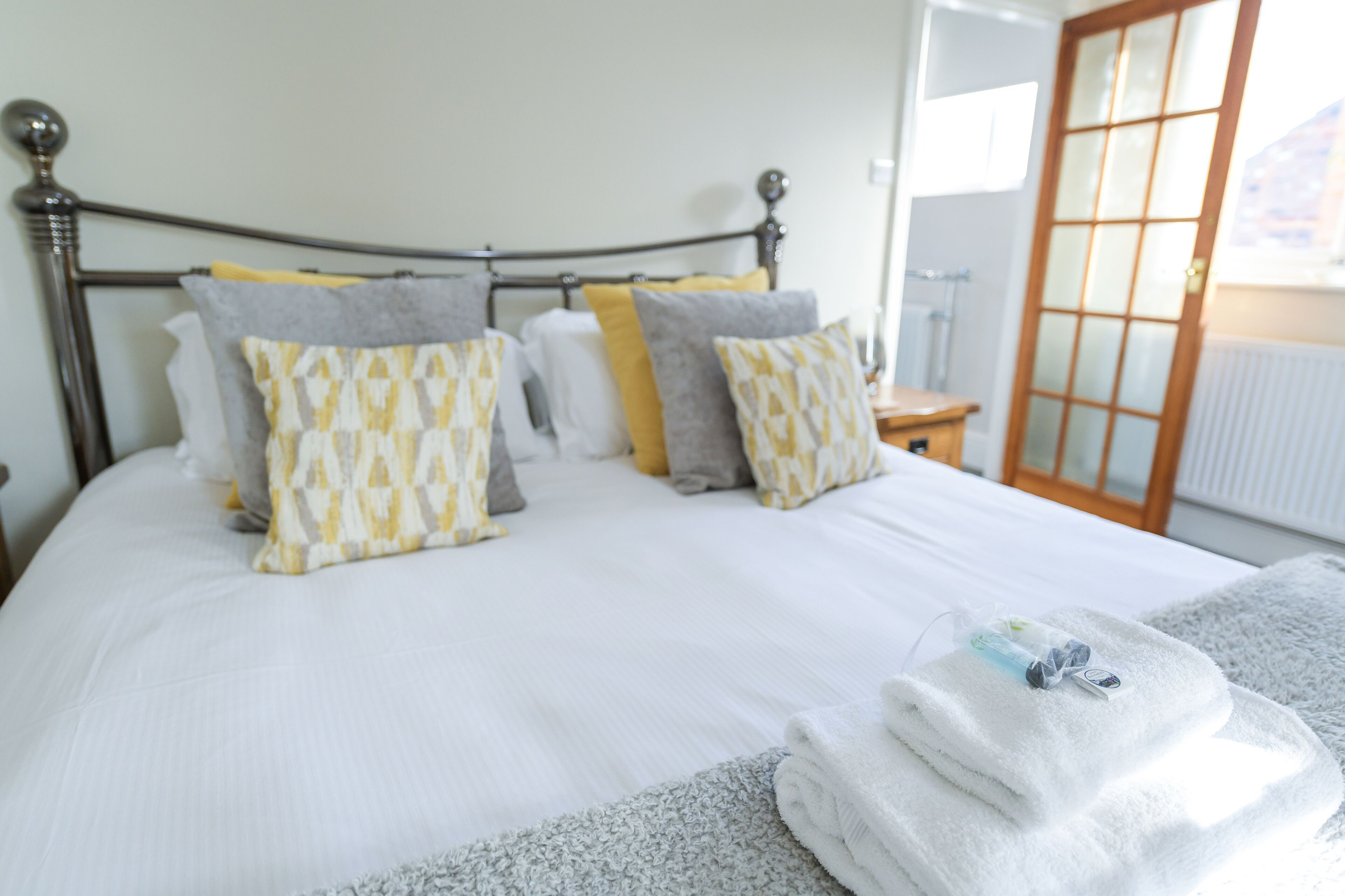 Una cama bien hecha con almohadas estampadas, una mesita de noche y vistas a una ventana con una puerta.