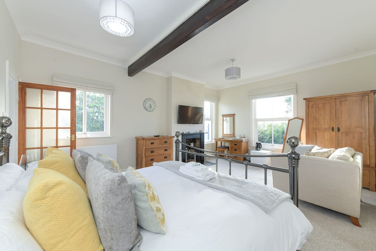 A bedroom with a large bed, a wooden wardrobe, a television, and a window with a view of greenery.