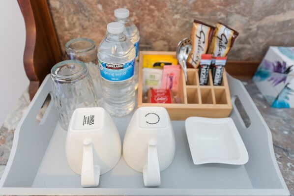 Una bandeja con una botella de agua, dos tazas blancas, un pequeño recipiente y una caja de aperitivos.