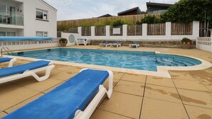 A swimming pool with blue lounge chairs, a white building, and a wooden fence. - 7 Europa Court (Newquay)