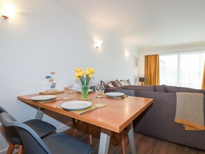 A dining area with a wooden table, chairs, and a vase of yellow flowers. - 7 Europa Court (Newquay)