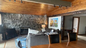 A cozy living room with a stone wall, a fireplace, a sofa, a coffee table, and a dining table.
