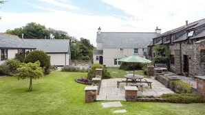 A courtyard with a stone patio, a green umbrella, and a wooden bench. - Honey Bee Cottage (Holsworthy)