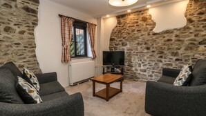A cozy living room with stone walls, two grey sofas, a wooden coffee table, and a flat-screen TV. - Honey Bee Cottage (Holsworthy)